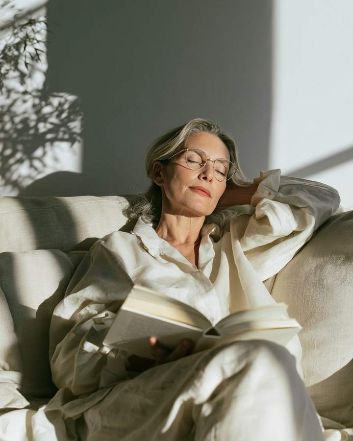Frau mit feiner Metallbrille liest entspannt auf dem Sofa